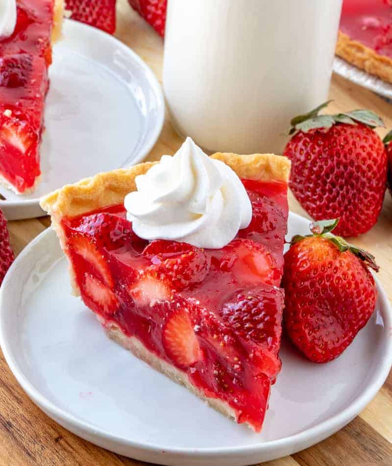Easy delicious and bursting with flavor this Strawberry Pie is an old-fashioned recipe that has minimal ingredients intense strawberry flavor and absolutely addicting. Strawberry pie on plate with whipped cream and milk on side