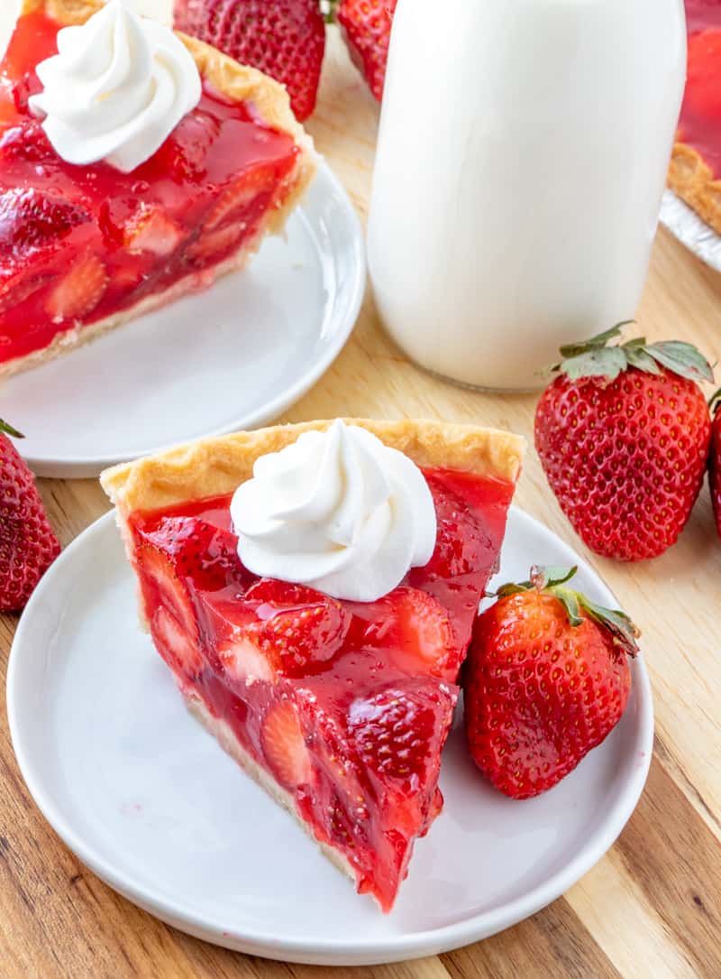 Easy delicious and bursting with flavor this Strawberry Pie is an old-fashioned recipe that has minimal ingredients intense strawberry flavor and absolutely addicting. Strawberry pie on white plate with whole strawberries and milk in background